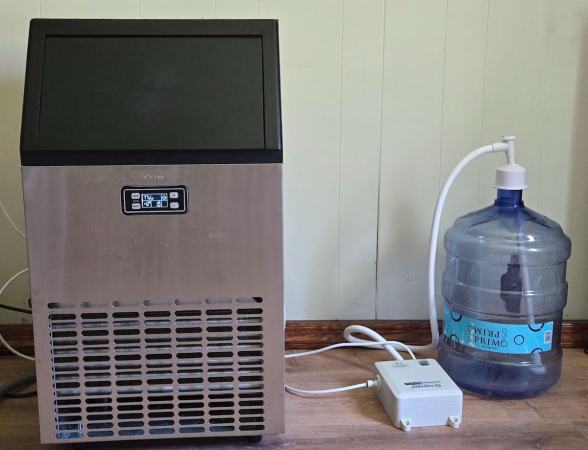 A commercial ice maker, a bottled water pump system, and a 5-gallon water jug are sitting on a garage floor.