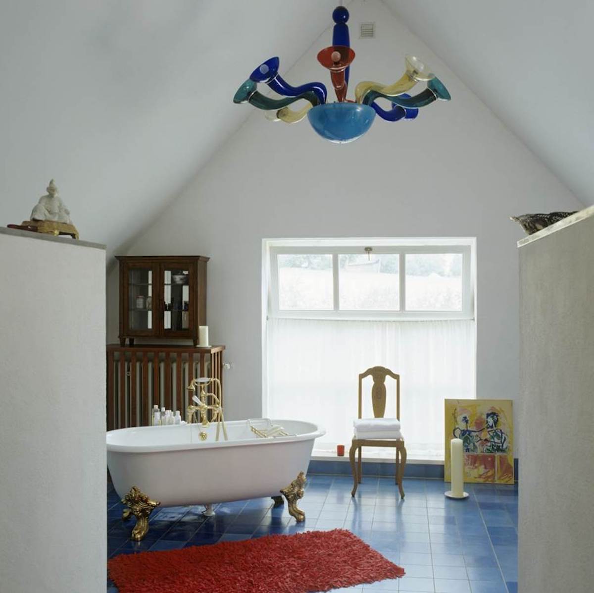 A white room with antique furnishings is capped by a multi-colored Murano glass chandelier.