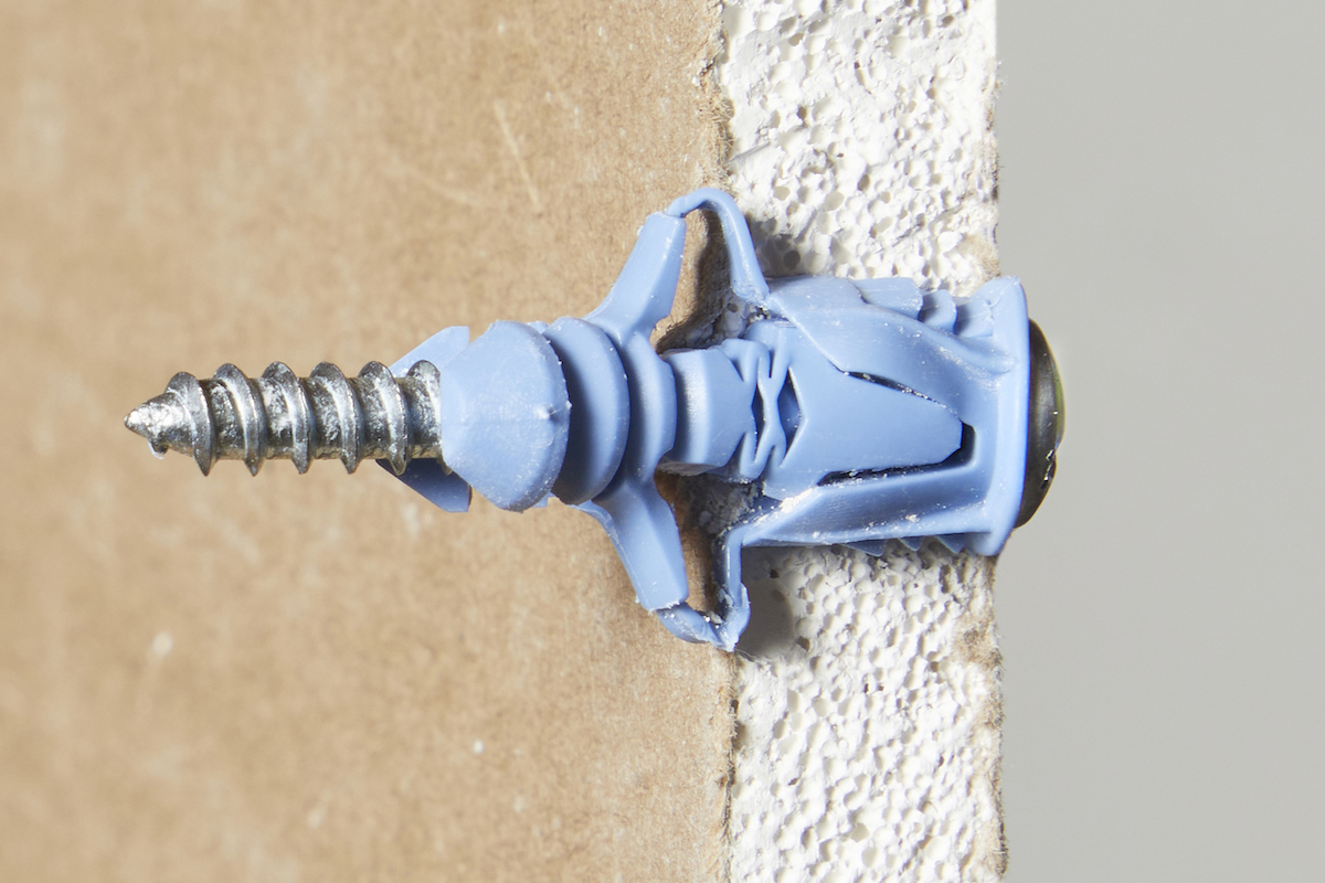 Side view of a plastic winged drywall anchor anchored in a piece of drywall.