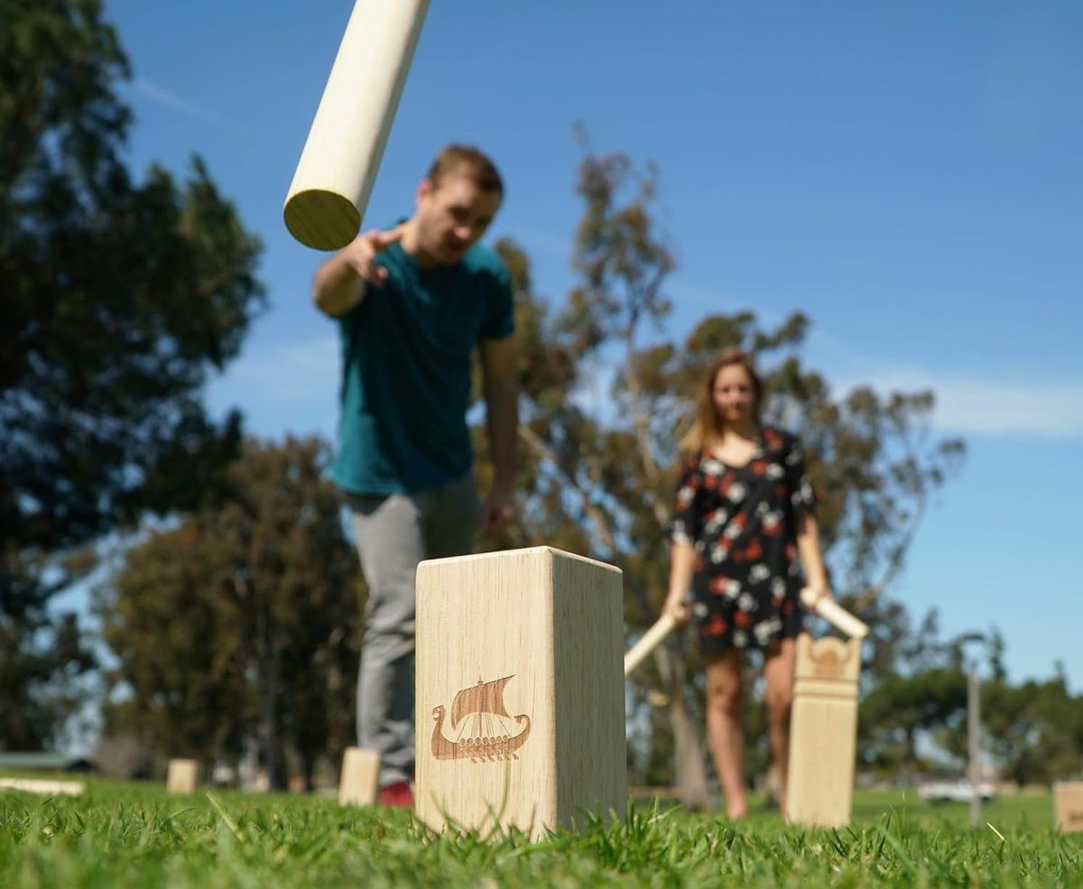 Two people playing Kubb wooden game in the yard.