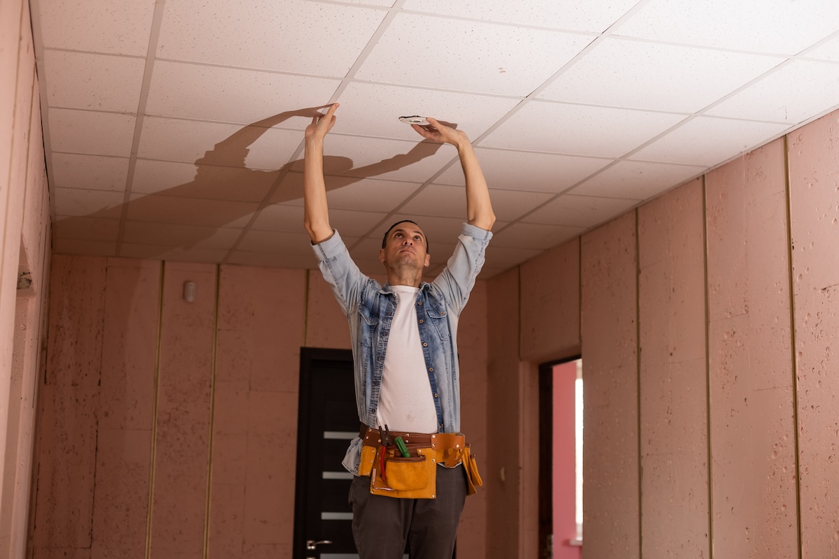 Repairman pushes on drop ceiling tiles.