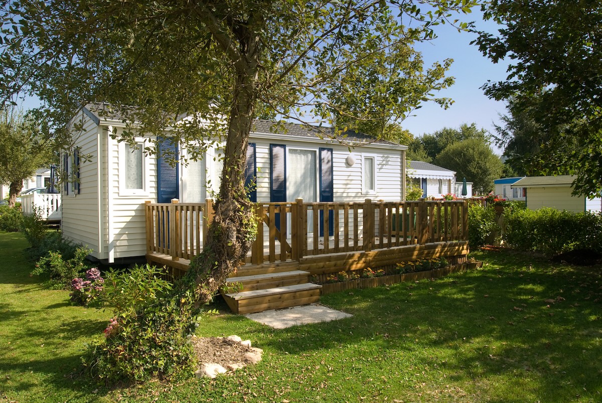 A white mobile home with built-on deck and blue windows shutters.