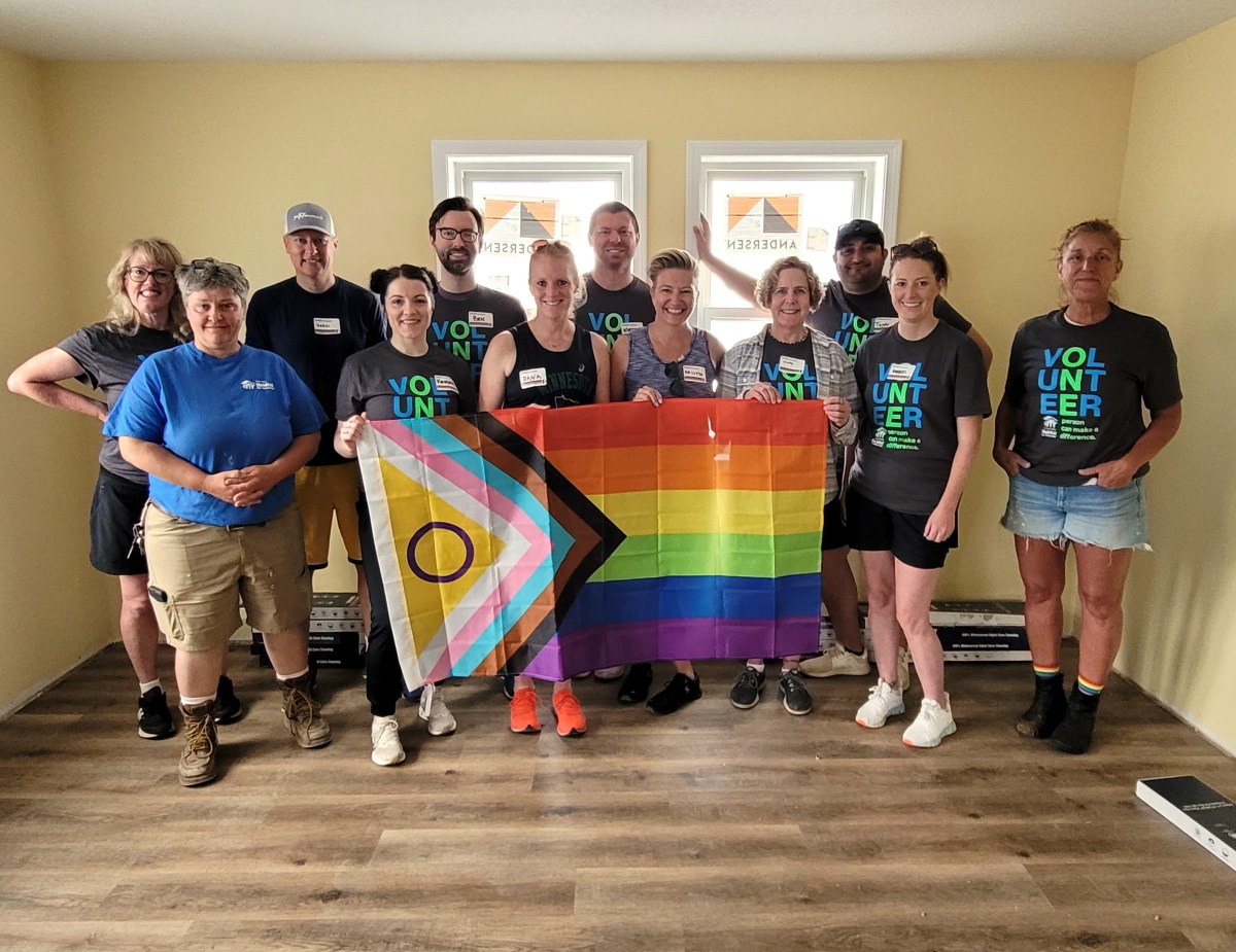 A group of volunteers holds a Pride flag during a Habitat for Humanity project.