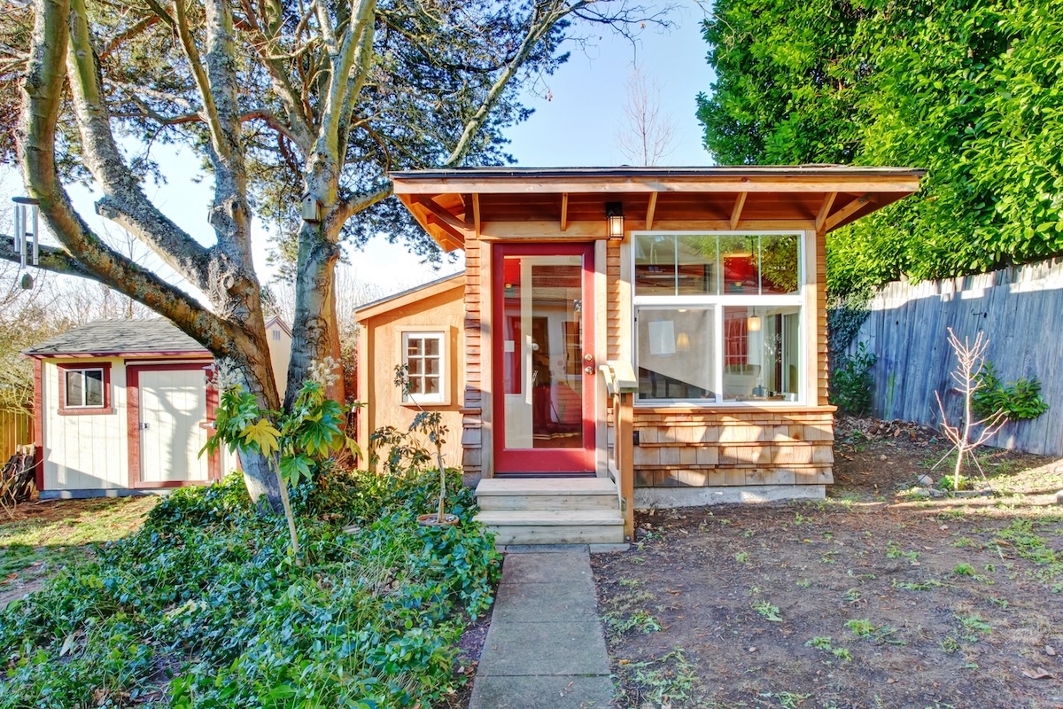 Tiny home made of light wood with windows and red front door.