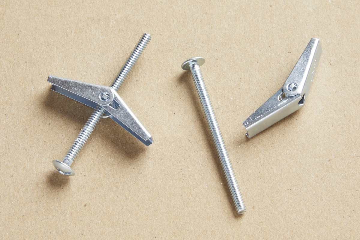 Two toggle bolt drywall anchors against a brown background.