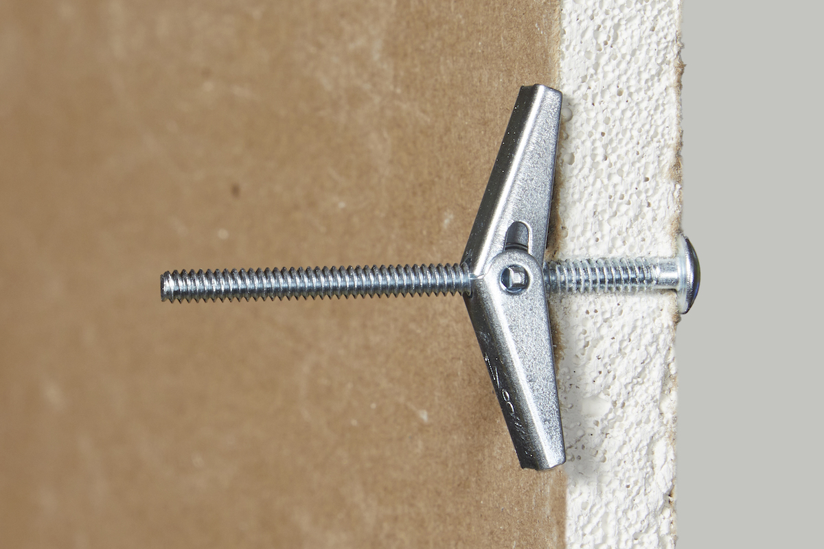 Side view of a toggle bolt drywall anchor inserted into drywall. 
