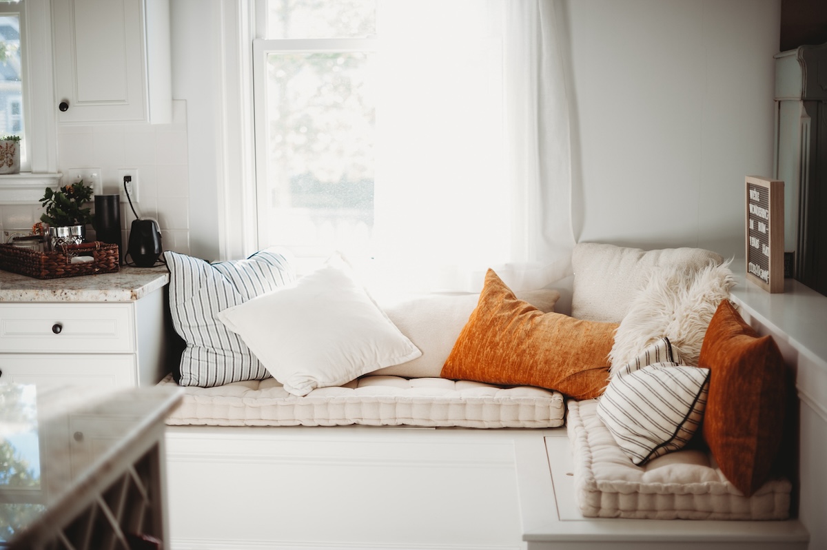 Cozy window seat with orange and white cushions with storage underneath.