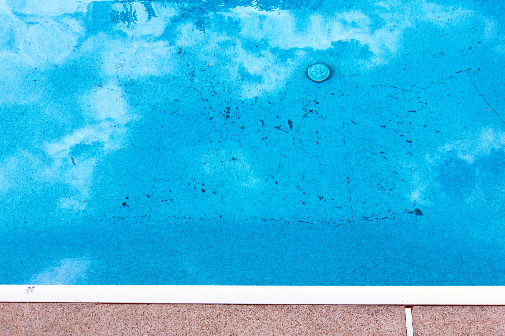 A mostly clean swimming pool with with many spots of visible black algae growth on its bottom.