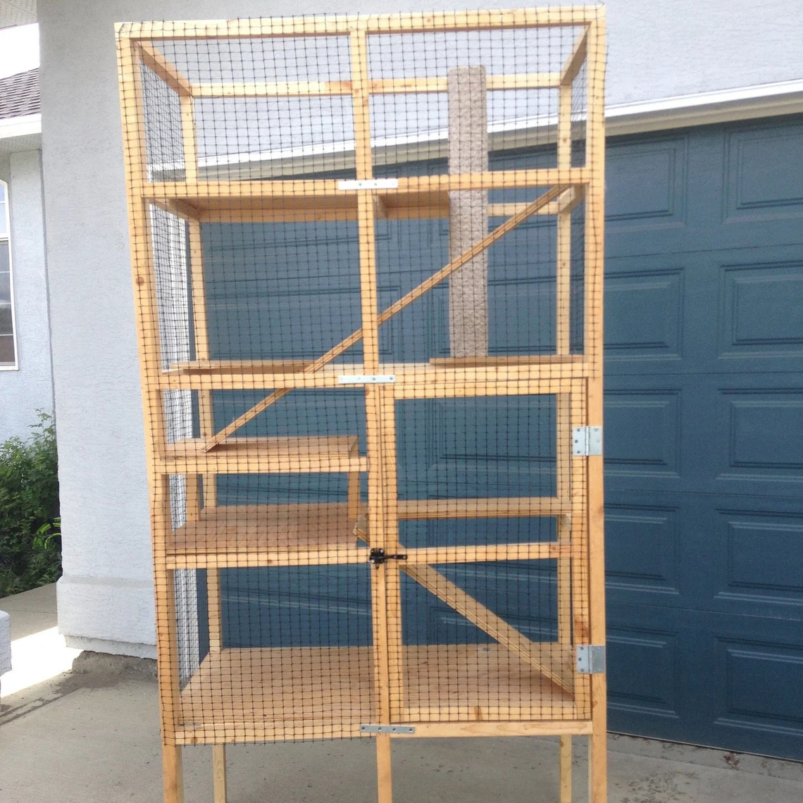 A tall catio with four levels and a door sits in a suburban driveway.