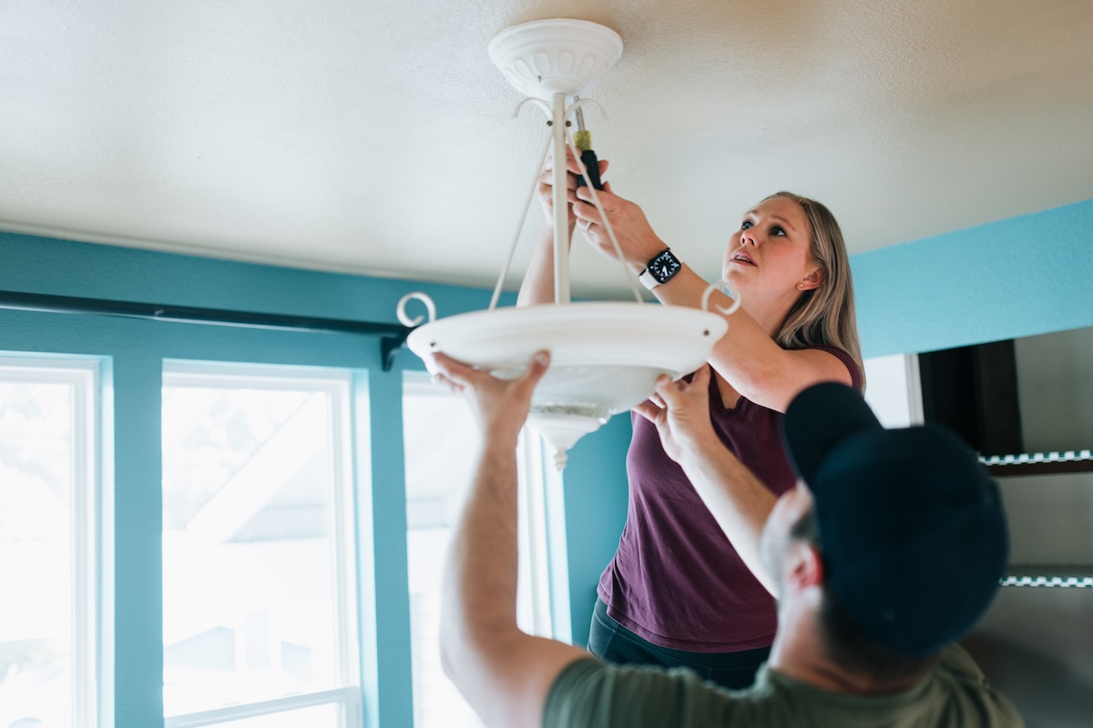 A young couple changes the lightbulb on a ceiling light fixture.