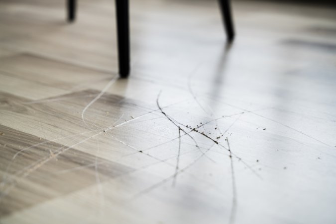 A light wood colored laminate flooring has a scratch that was caused by the chair on top of it.