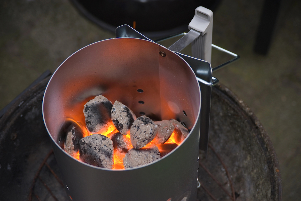 Charcoal chimney full of glowing charcoal sitting on top of a grill. 