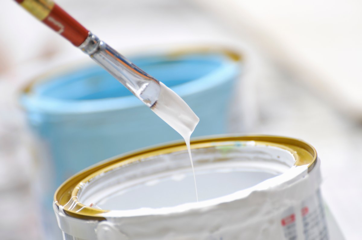 Paint brush dipping inside a can of white paint.