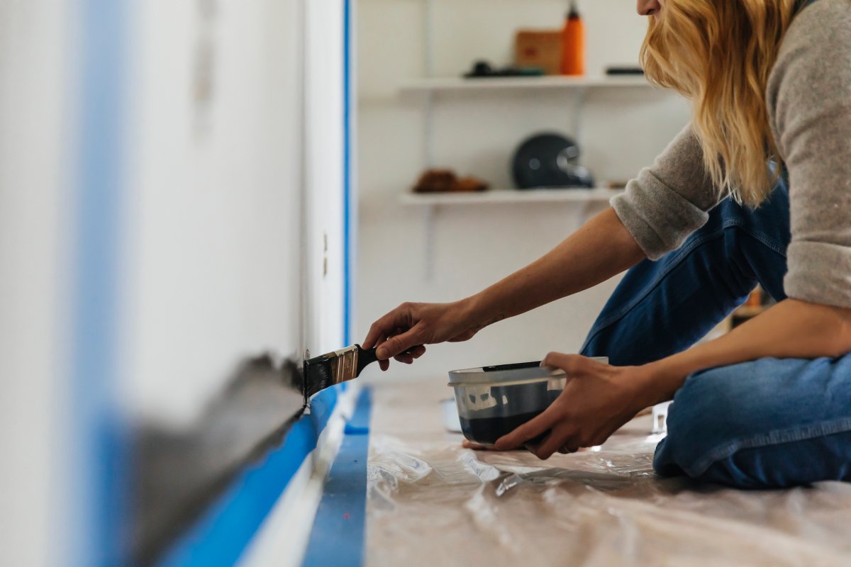 Woman sitting on floor painting a wall white.