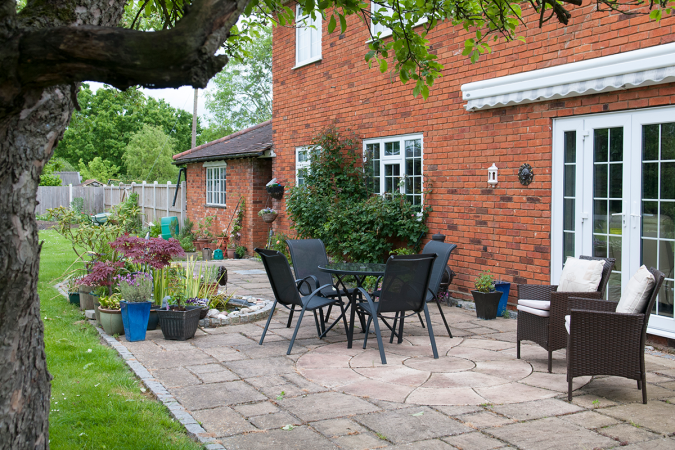 A residential backyard with a paver patio, outdoor furniture, plants, and more.