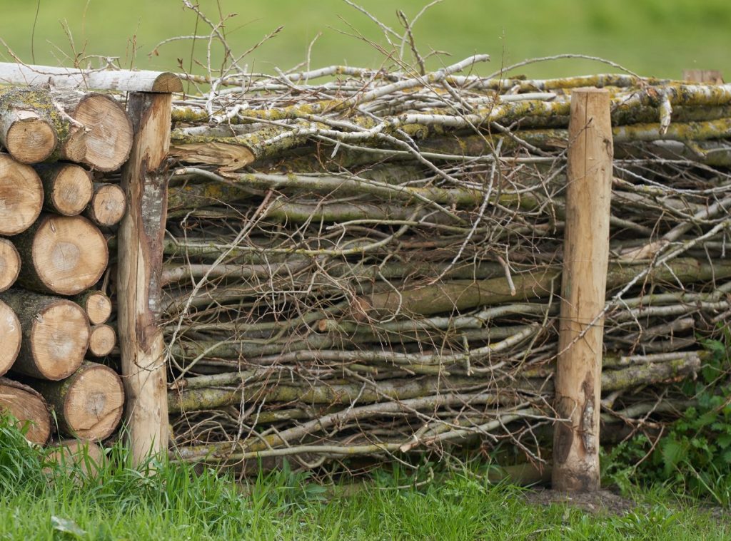 A dead hedge fence made with plant debris, logs, and twigs.