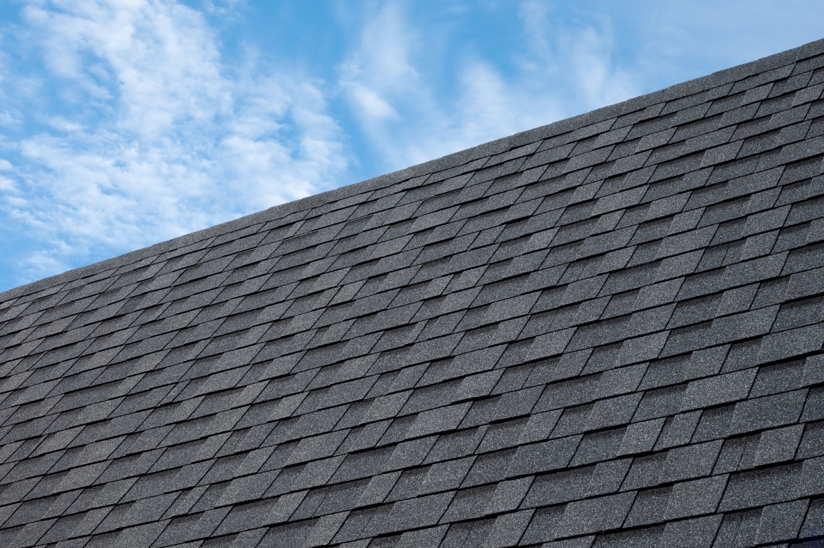 New roof shingles installed on roof with blue sky background.