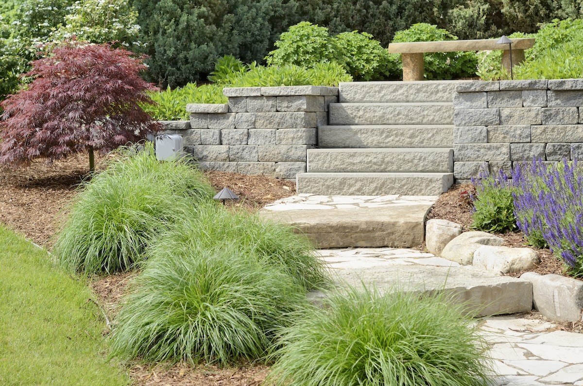 Sustainable hardscaping in a residential outdoor space with a retaining wall, stairs, and a permeable stone pathway.