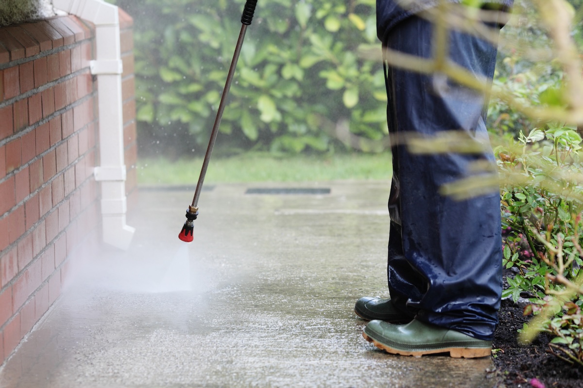 A person using a pressure washer to clean concrete driveway stains and concrete sidewalk stains.