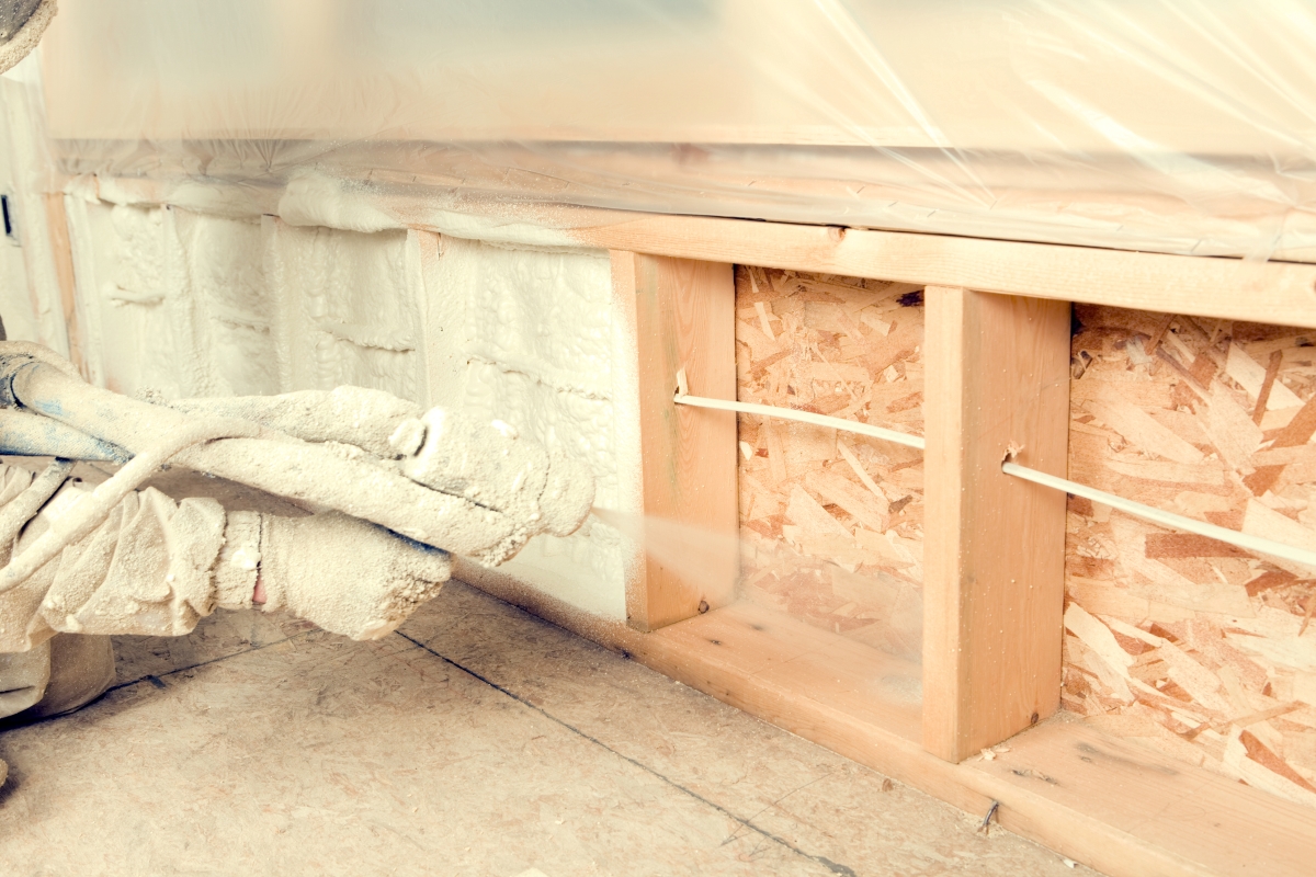 A person is spraying expandable foam insulation between wall studs.