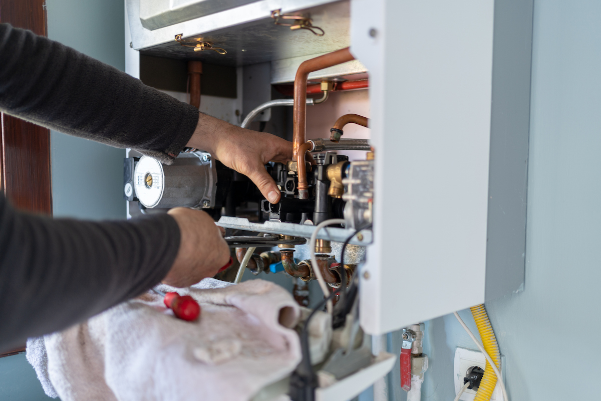 A person is using tools inside of an open tankless water heater.