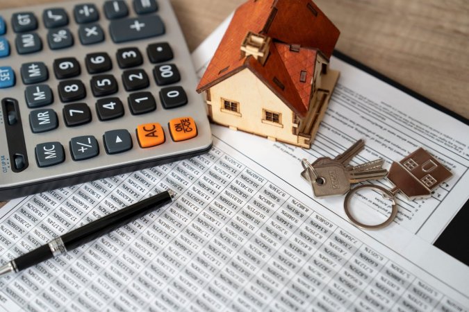 A close up of a document, a small model house, a pen, keys, and a calculator.