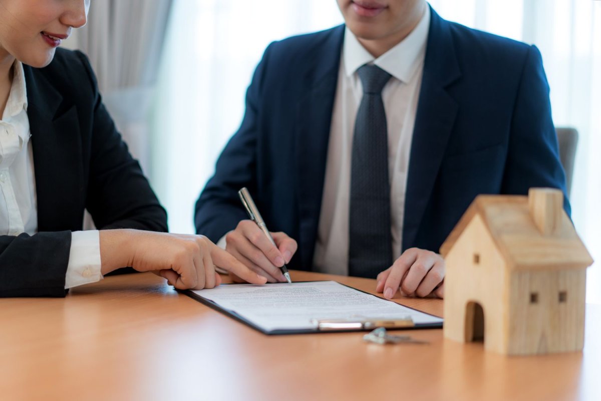 Two people sit at a table and review documents as a small model house sits on the table. 