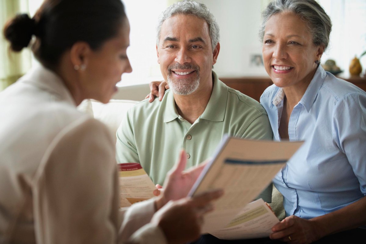 Three people smile as one of the woman shows the two others across from her a document.