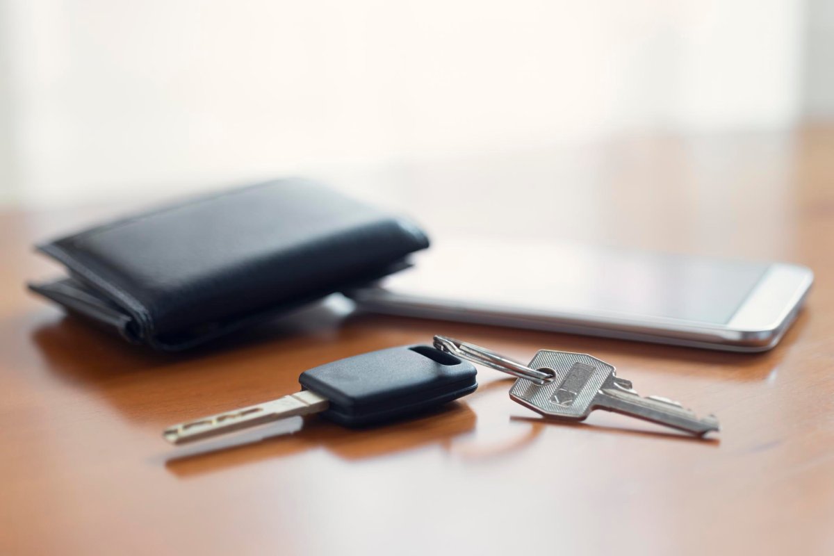 A close up of a set of keys with a wallet and phone in the background. 