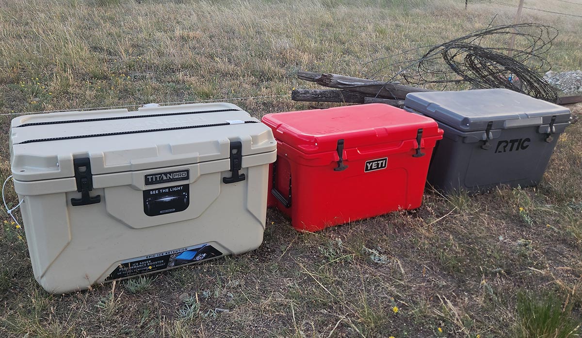 White Titan, Gray RTIC, and Red Yeti coolers sitting on grass