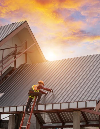 A roofer on a ladder works on a roof at sunrise. 