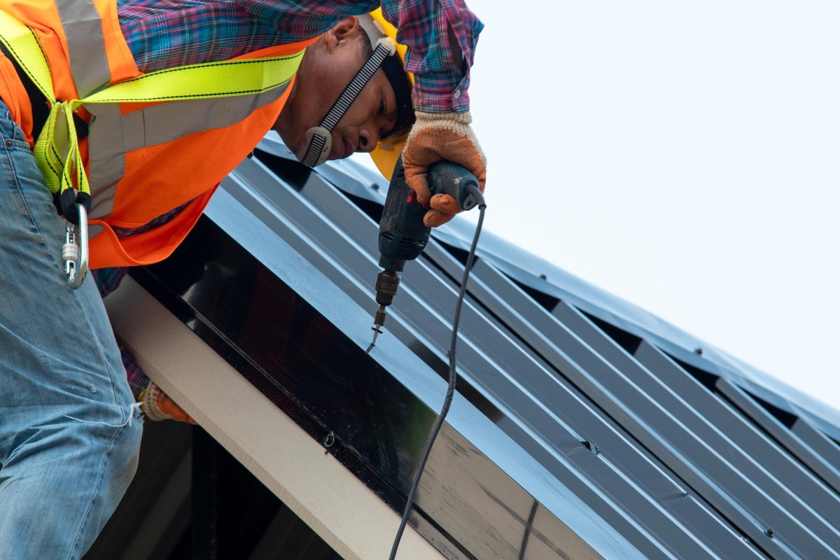 A close up of a worker drilling into roofing material. 