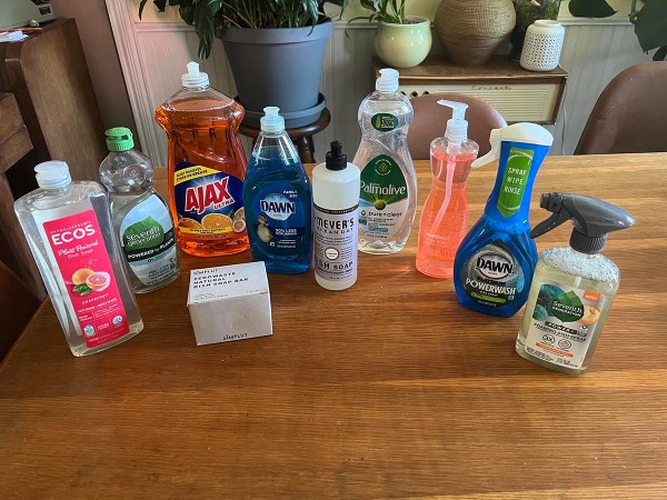 Nine bottles and one bar of the best dish soap on a wood table