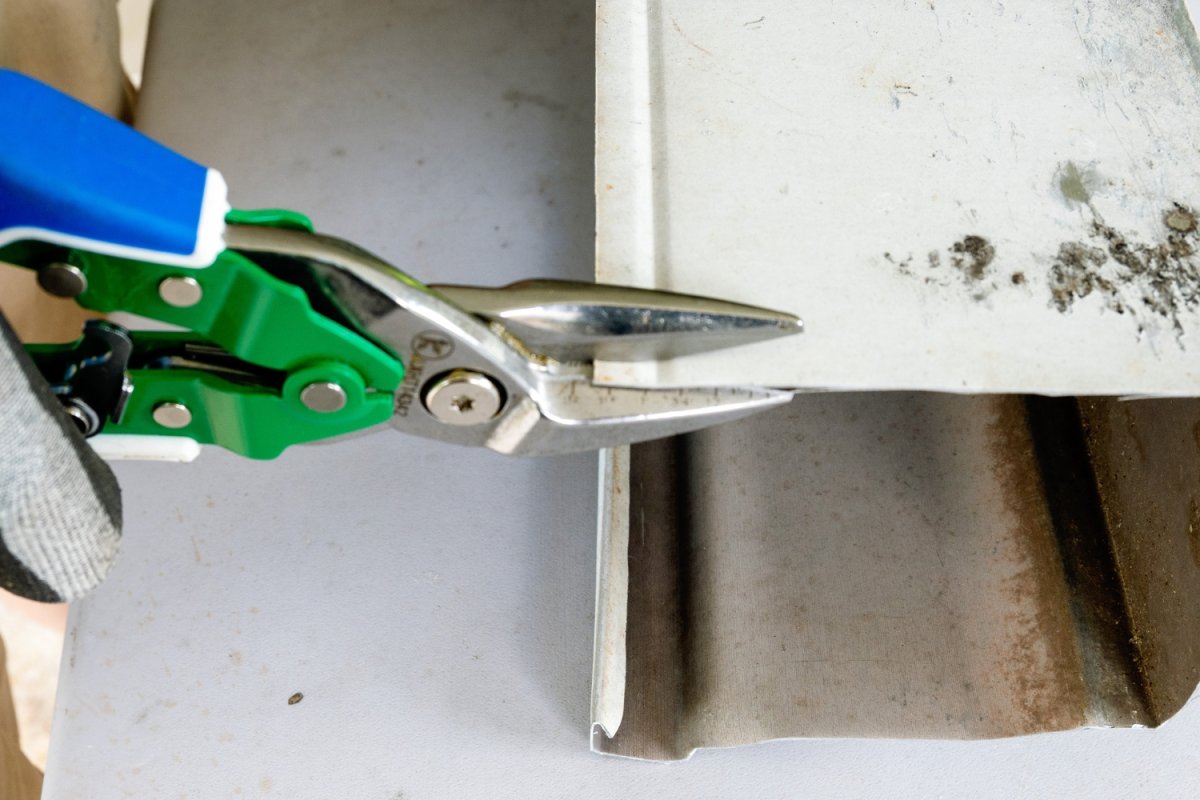 Person cutting through gutter material with green Lenox tin snips