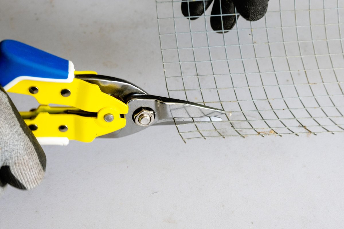 Person cutting through chicken wire with yellow Lenox aviation tin snips