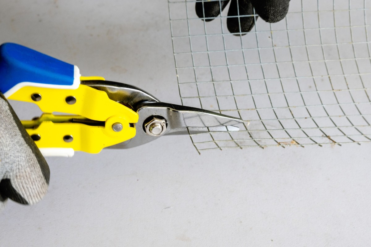 Person cutting through chicken wire with yellow Lenox aviation tin snips