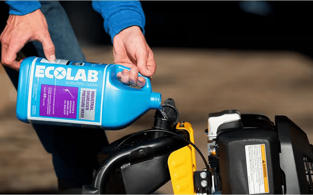 A person filling a pressure washer with Ecolab industrial degreaser solution for cleaning concrete.
