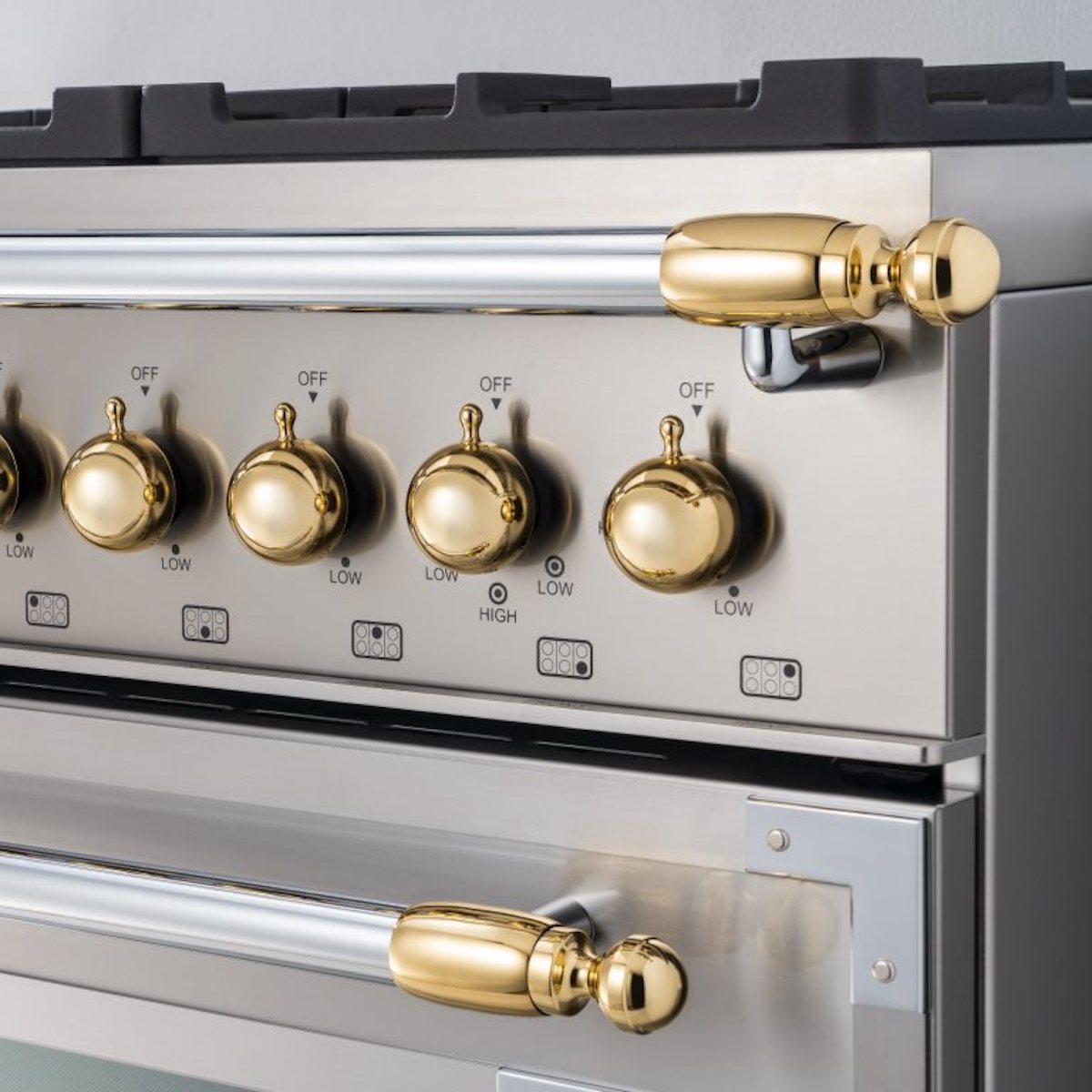 Close up view of gold knobs and handle finials on a stainless steel Bertazzoni range.