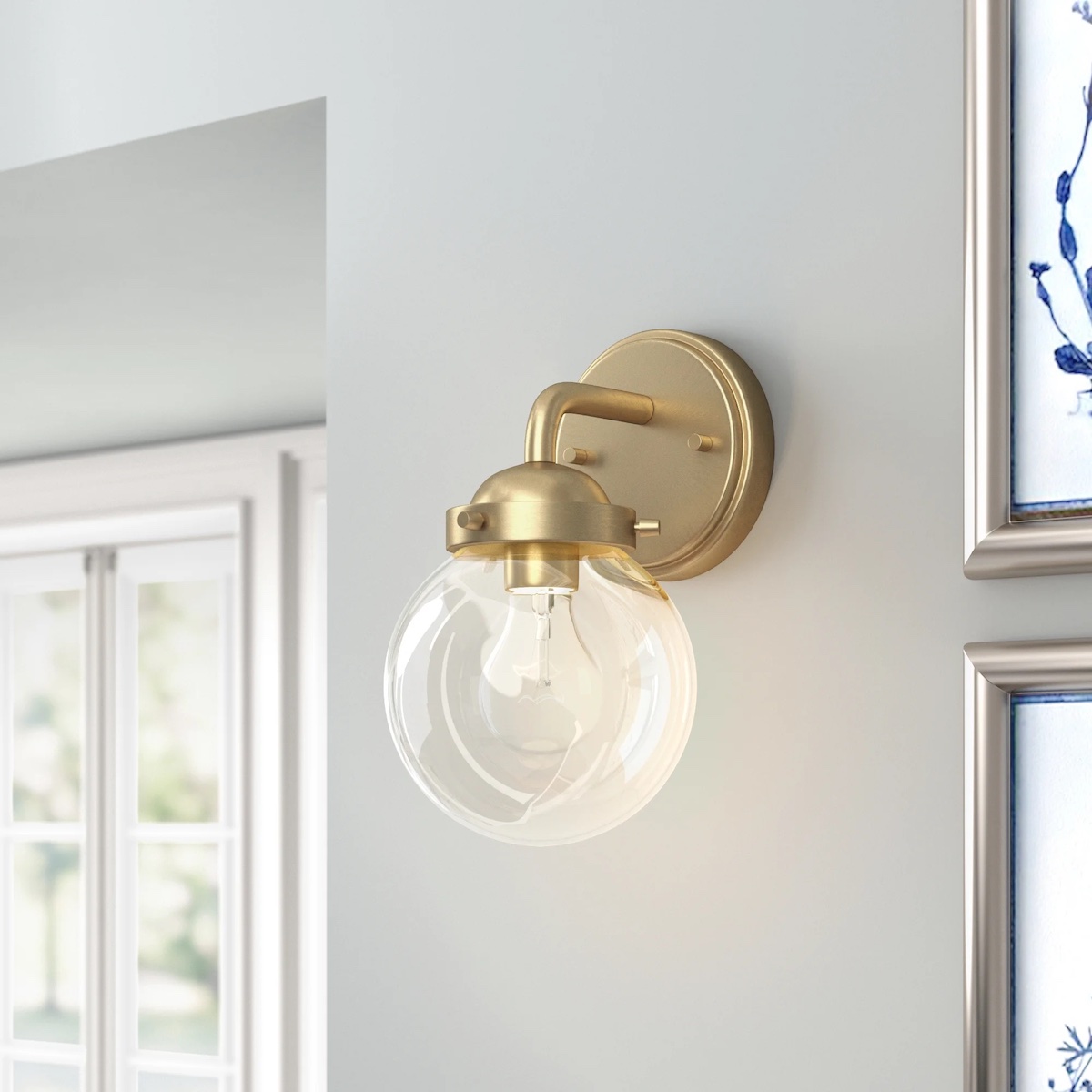 Brushed gold sconce with a glass globe fixture attached to a round metal plate.