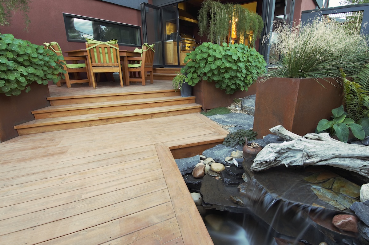 A modern deck with planters and a stone-circled pond. 