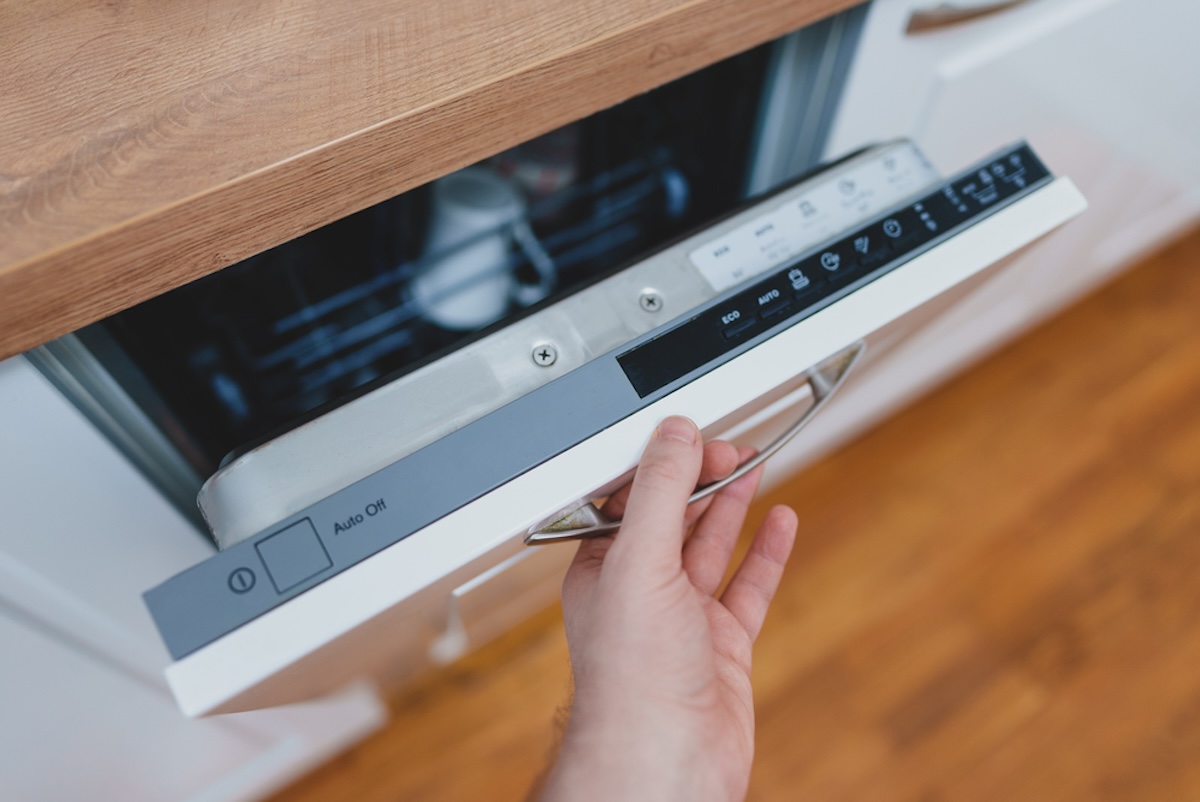 Man checks dishwasher settings on white dishwasher above light hardwood floors.