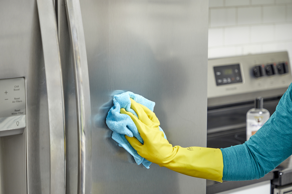 Woman uses a microfiber cloth to rub mineral oil into her stainless steel refrigerator.