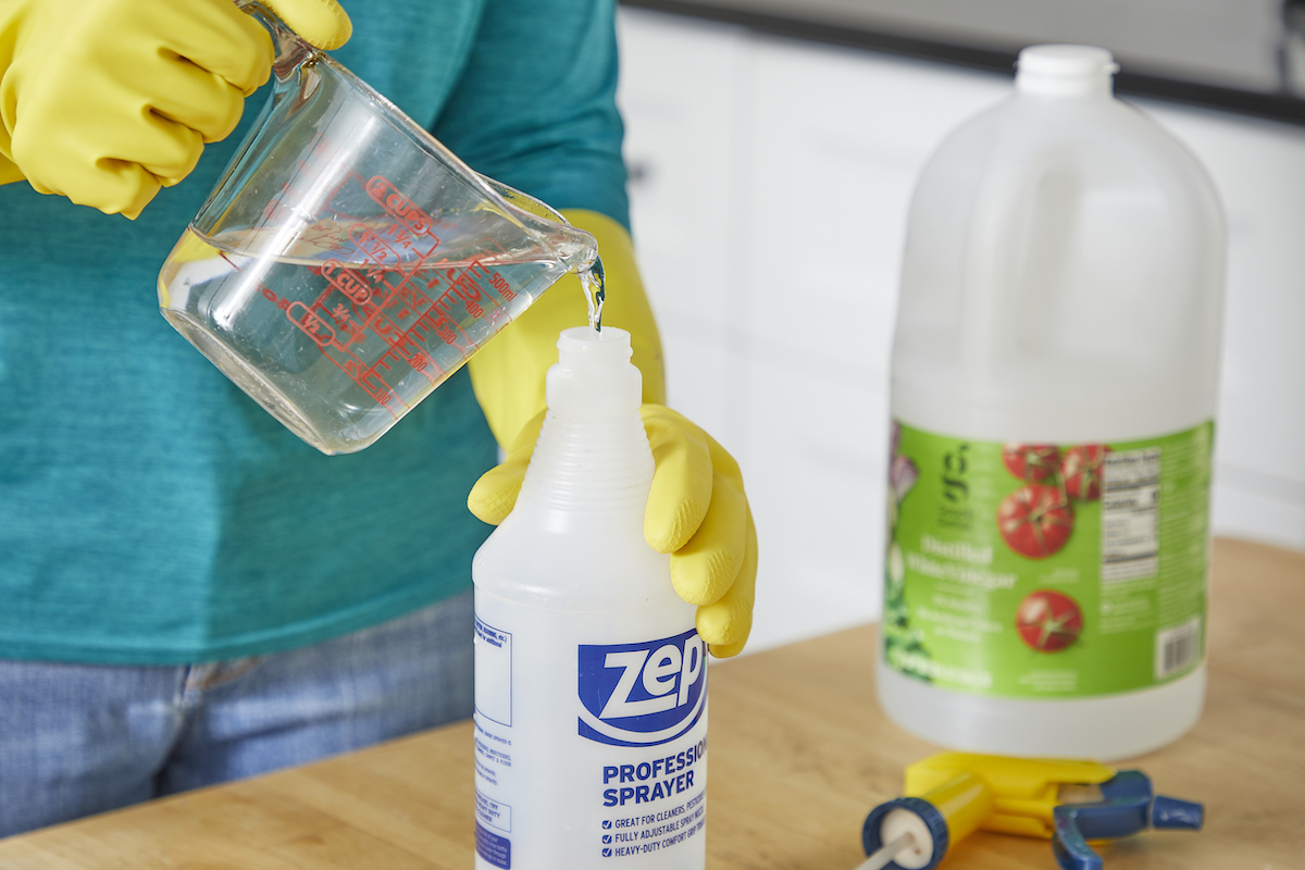 Woman fills spray bottle with vinegar from a measuring cup.