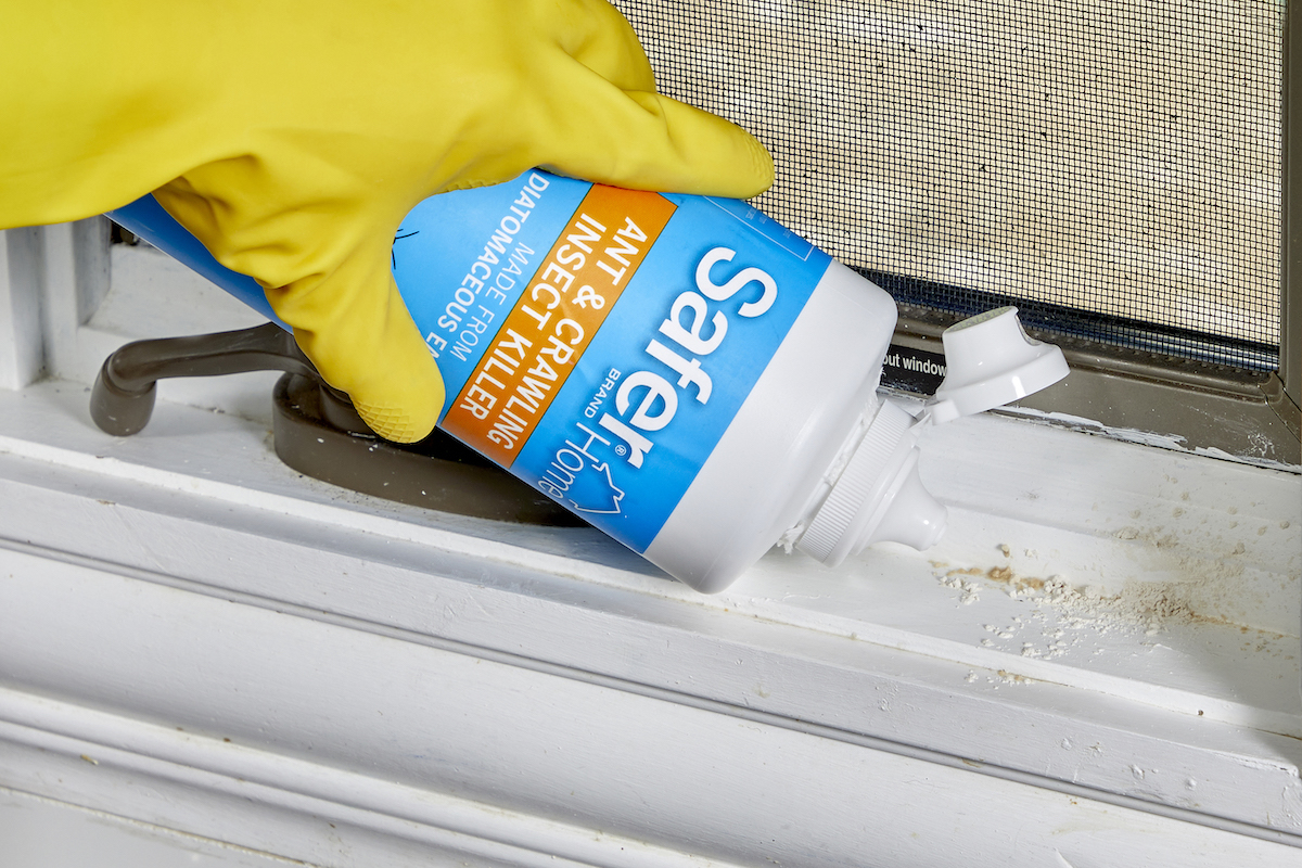 Woman wearing yellow rubber gloves applies diatomaceous earth to her window sill. 