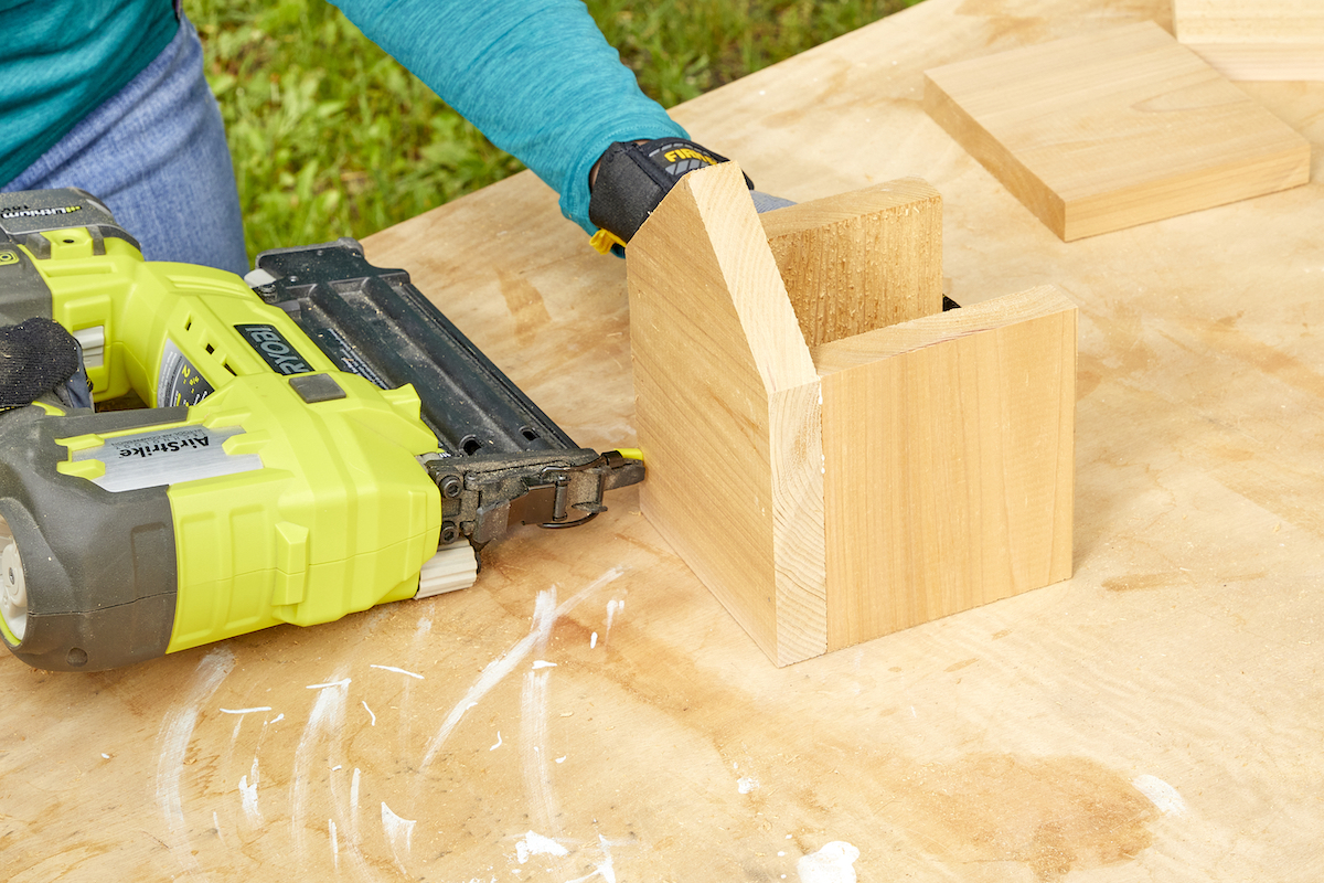 Woman uses a nail gun to attach the sides of a birdhouse to the front.