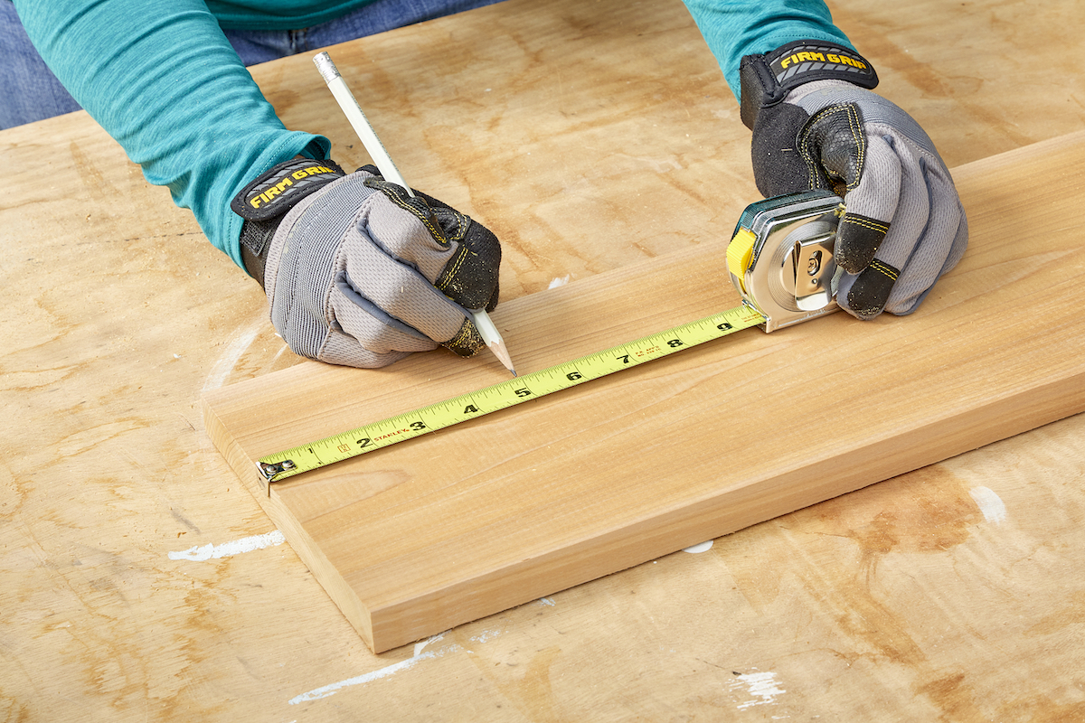 Woman measures a board with a measuring tape and marks the 5-inch mark.