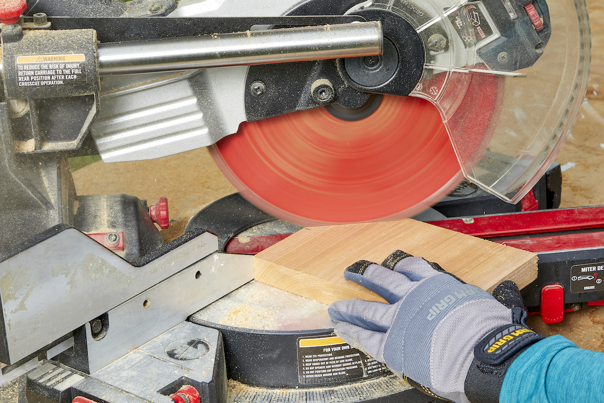 Woman uses a miter saw to cut a piece of wood at a 45-degree angle.