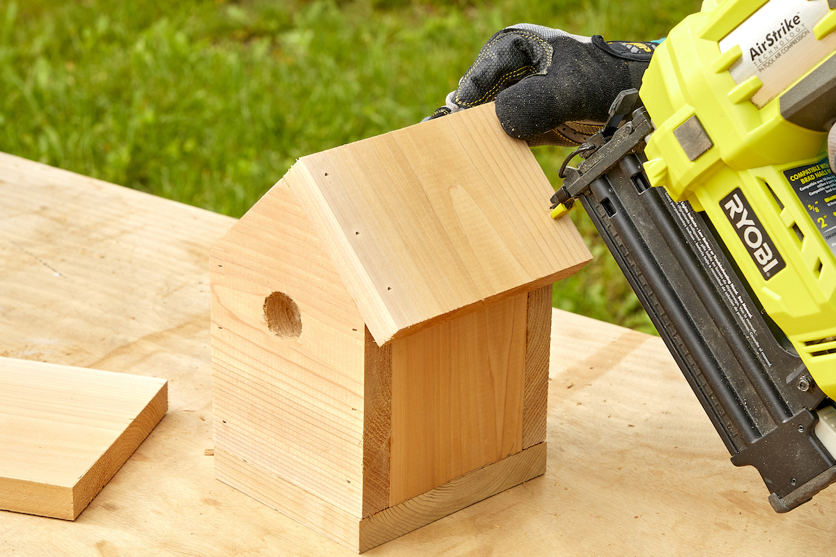 Woman uses a nail gun to nail the roof onto a birdhhouse.