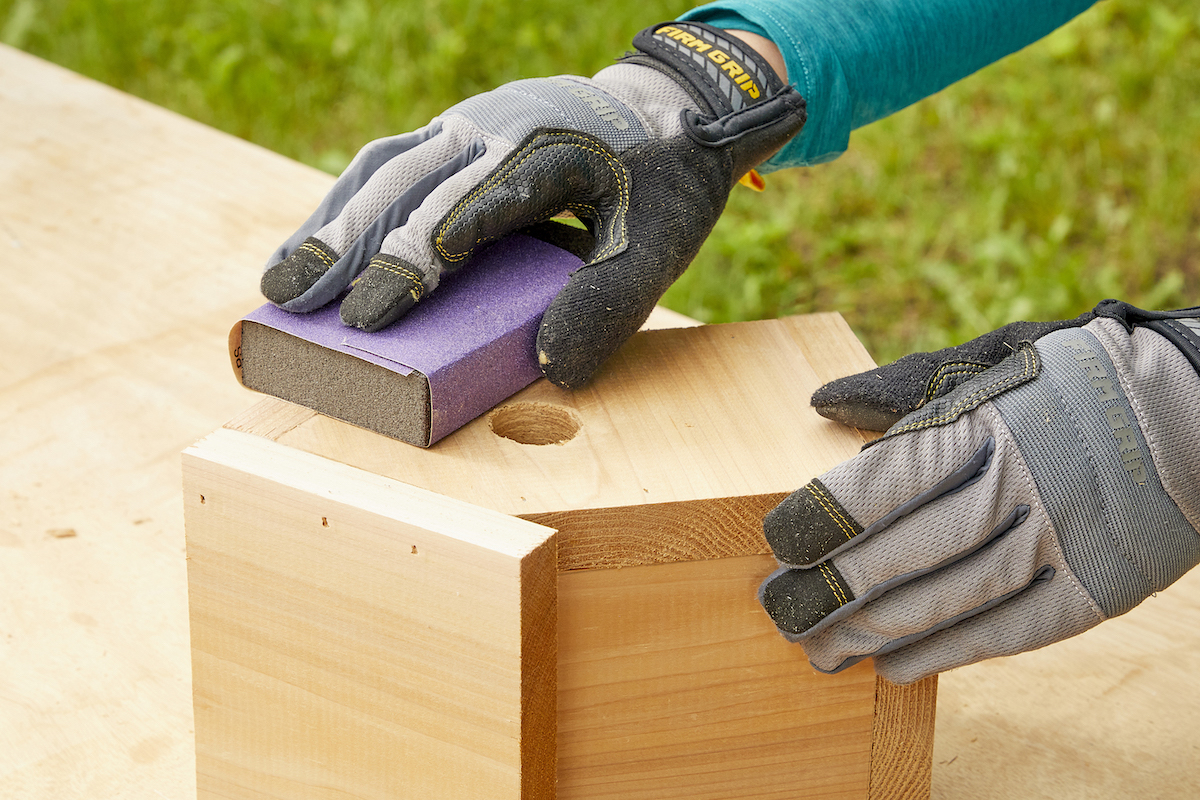 Woman uses a sanding block to sand a handmade birdhouse.