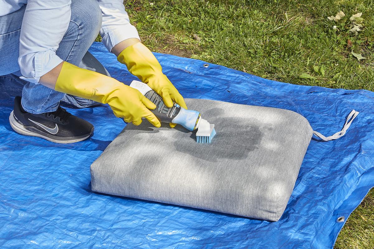 Woman uses Carbona outdoor cleaner on patio cushions.